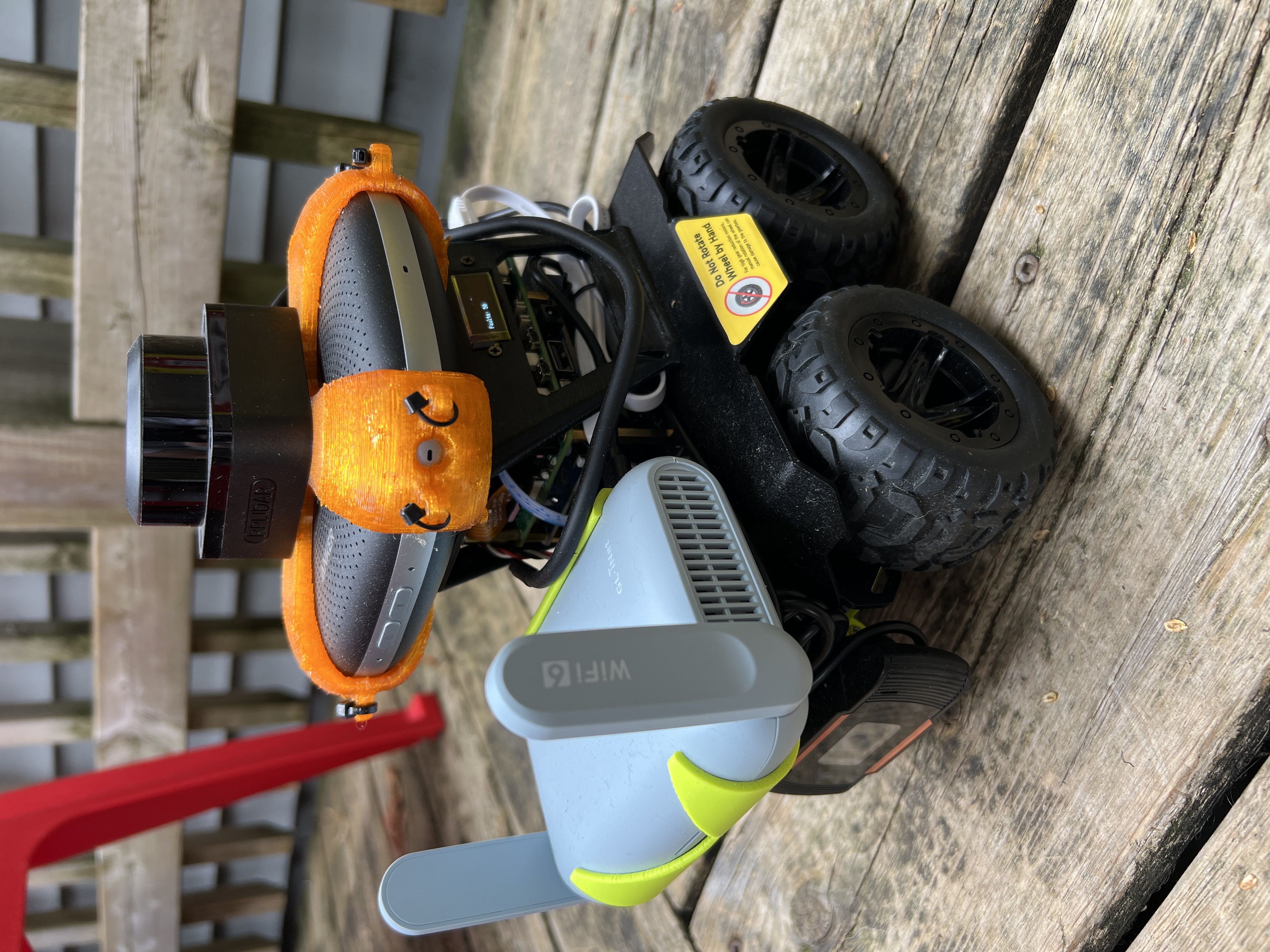 Four-wheeled pi-bot rover with lidar, orange printed mounts, exposed electronics and a Wi-Fi router.